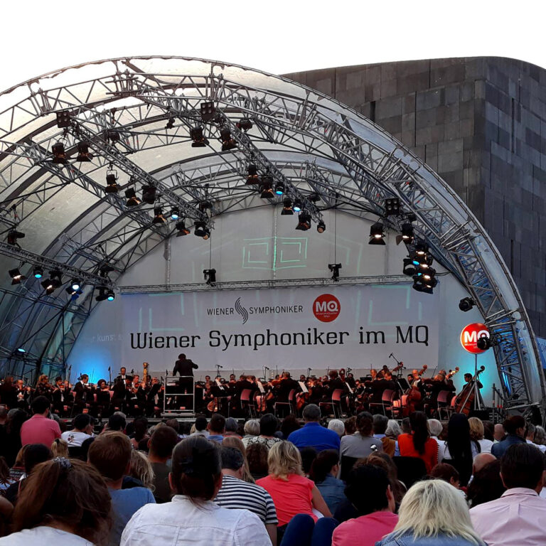 audience sitting in front of orchestra in the open air
